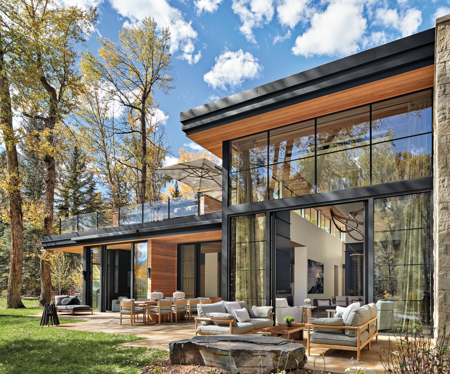 Modern glass and stone home with outdoor terrace under autumn trees