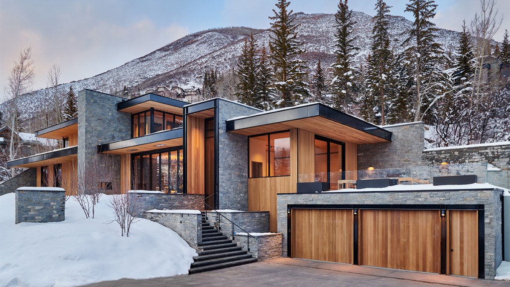 Contemporary mountain home with stone and cedar against a snowy hillside