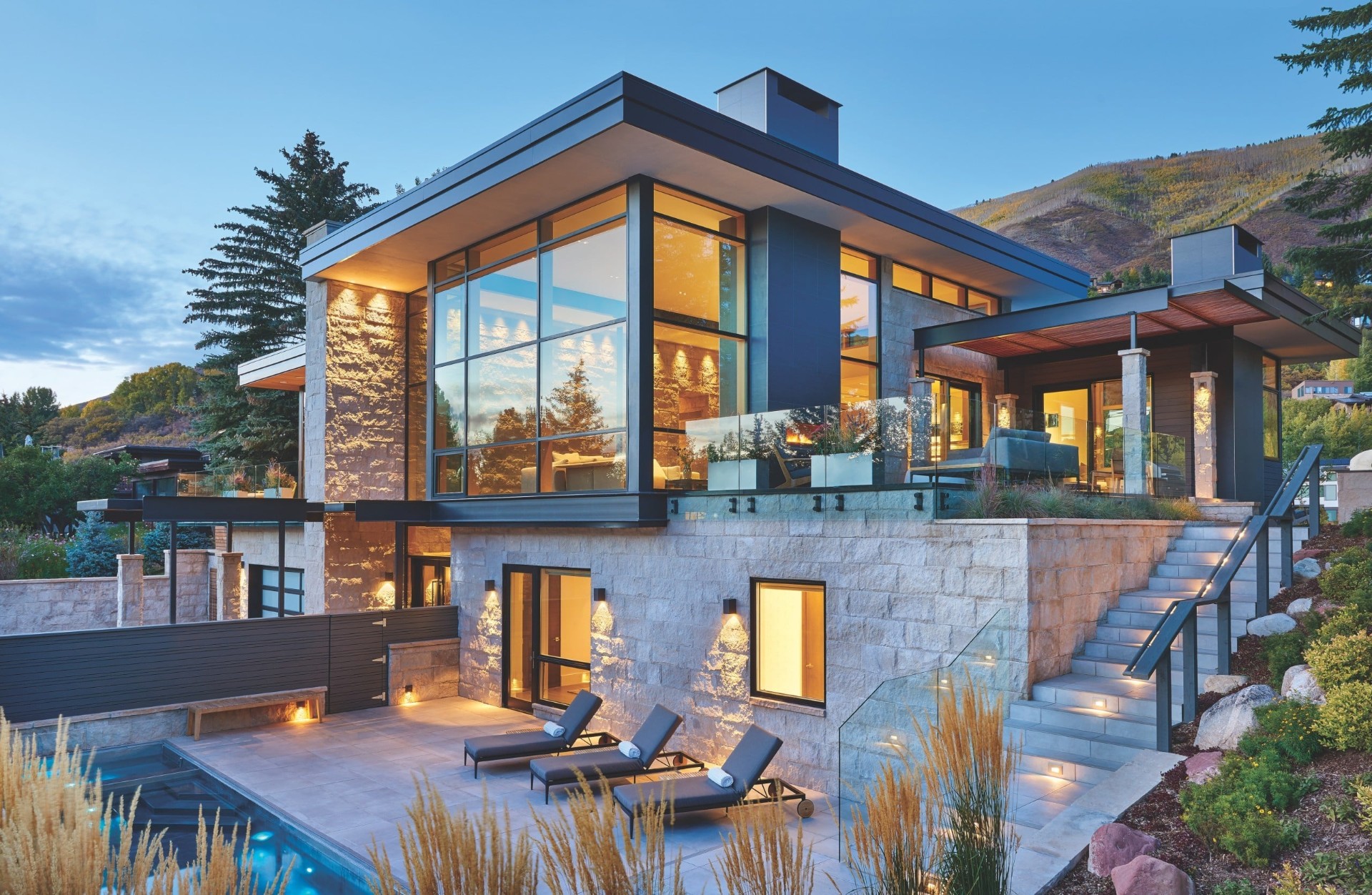 Modern stone home glowing at twilight with poolside terrace